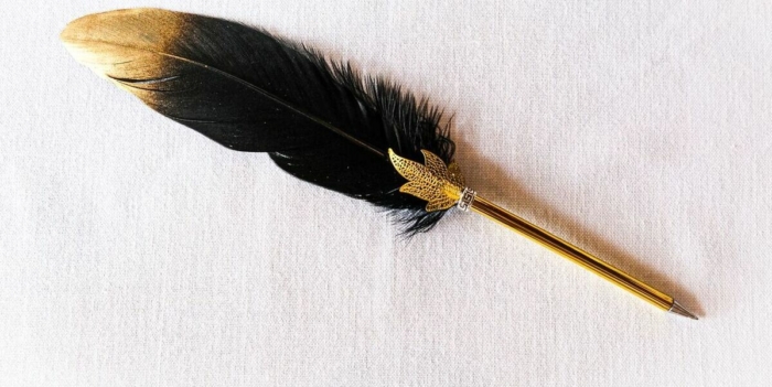 A vintage-style feather pen with gold accents lying on a white surface
