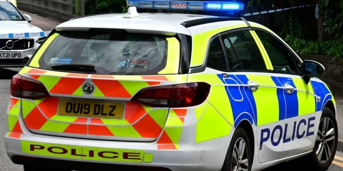 Back view of a British police car with flashing blue lights on a city road, ensuring law enforcement