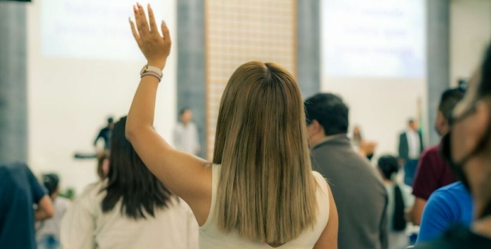 Back view of a woman raising hand during an indoor event, showcasing engagement.