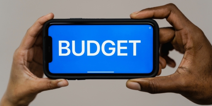 Two hands hold a smartphone displaying the word 'budget' on a blue screen,